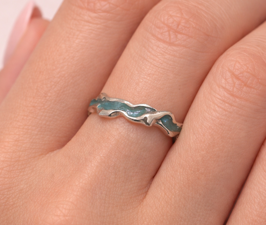 Silver ring with blue accents on a person's finger against a light pink background
