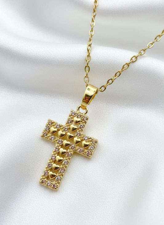 Gold cross pendant with heart designs on a white background