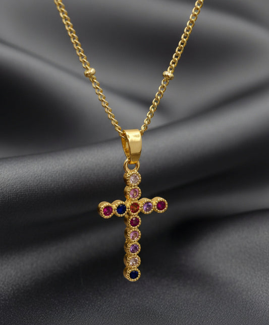 Gold cross pendant with colored gemstones on a light pink background