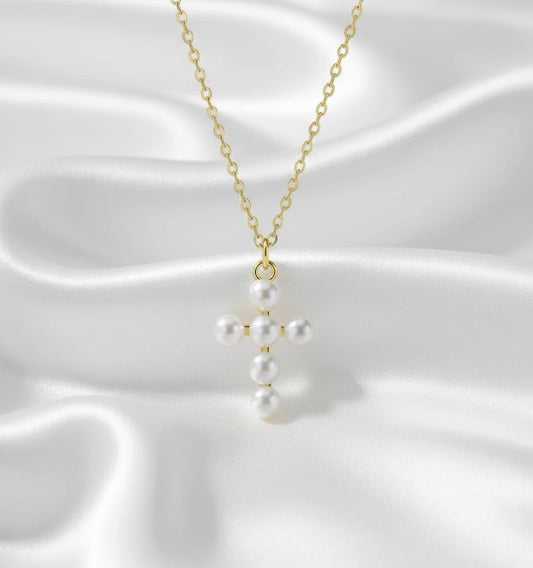 Pearl cross pendant on a gold chain against a white background