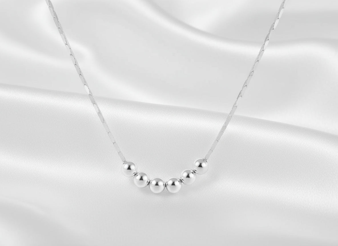Silver necklace with five evenly spaced beads on a white background