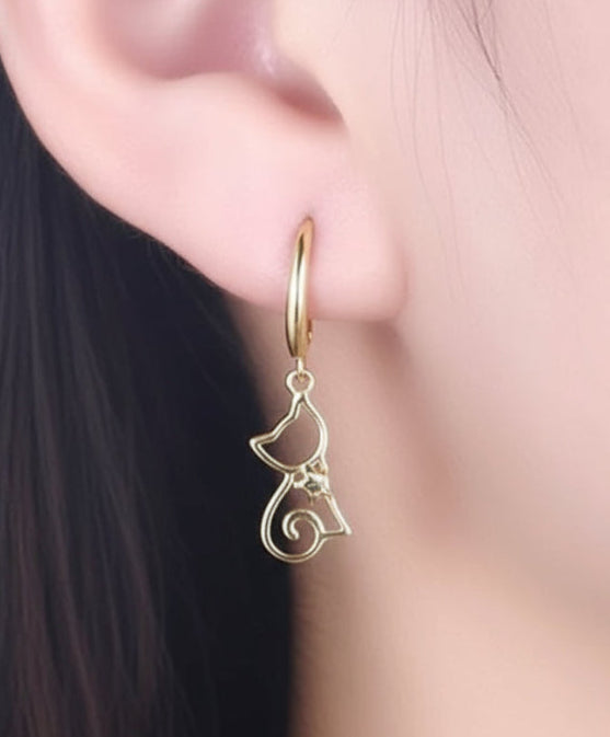 Gold hoop earring with cat-shaped pendant worn by a person.