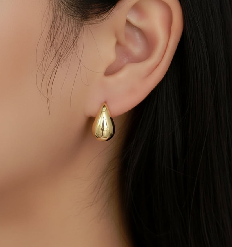 Gold teardrop earring worn on an ear with dark hair in the background
