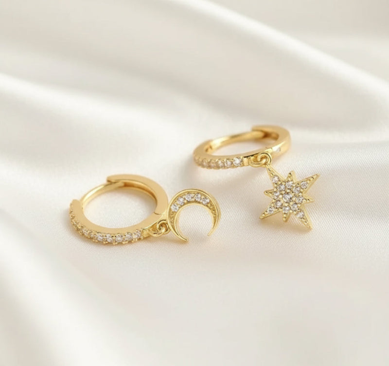 Gold hoop earrings with star and moon charms on a white background