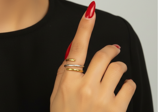 Hand with red nail polish and gold rings on a plain background