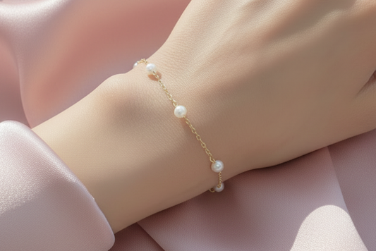 Gold bracelet with pearls on a wrist against a neutral background