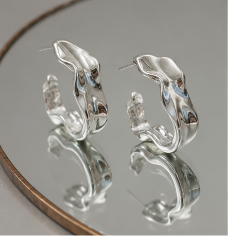 Silver hoop earrings on a reflective surface with a neutral background