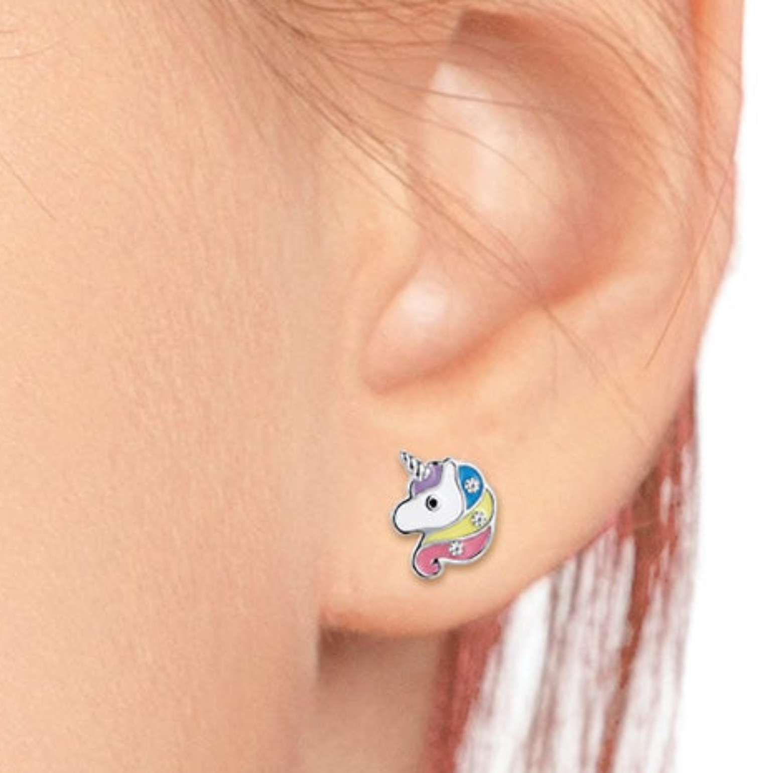 A close-up of a person's ear wearing a small colorful unicorn stud earring. The earring features a white unicorn face with a blue horn and pastel blue, pink, yellow, and purple details.
