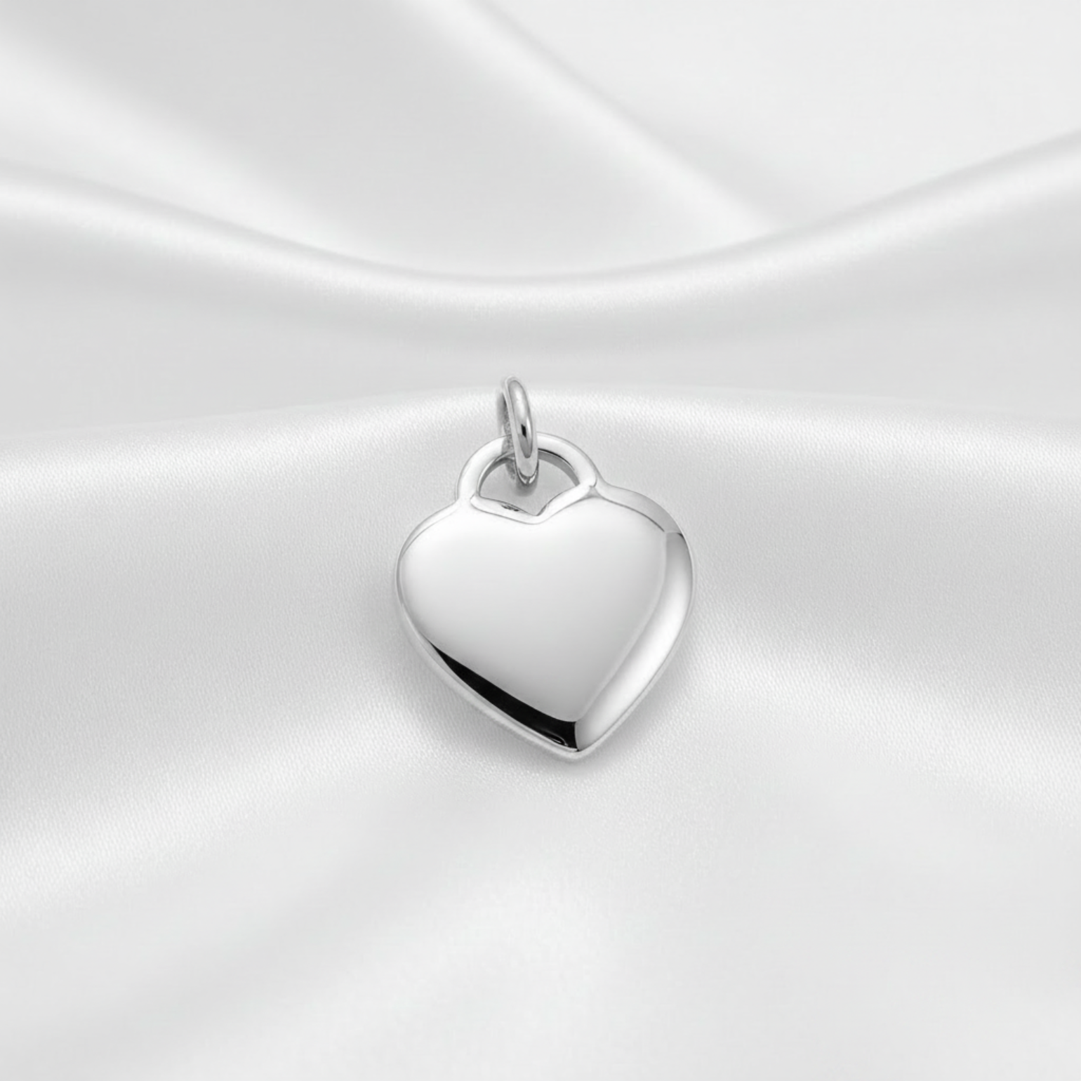 A polished rhodium-plated heart-shaped pendant charm with a small top loop, displayed on draped white satin fabric. The text 'Rhodium PLATED' is visible in the bottom right corner.
