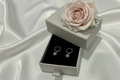 Pair of silver earrings in a gray jewelry box on a white surface with a keyboard in the background.