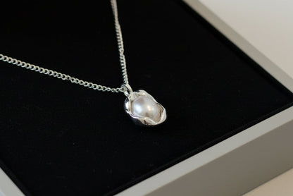 Silver necklace with a pendant in an open jewelry box on a light surface.