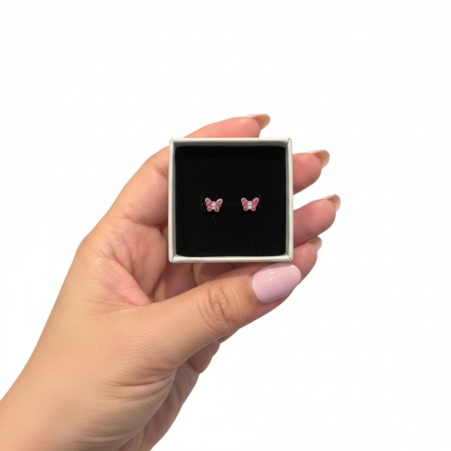 A hand holding a small jewelry box with a black velvet insert, displaying a pair of pink butterfly stud earrings.