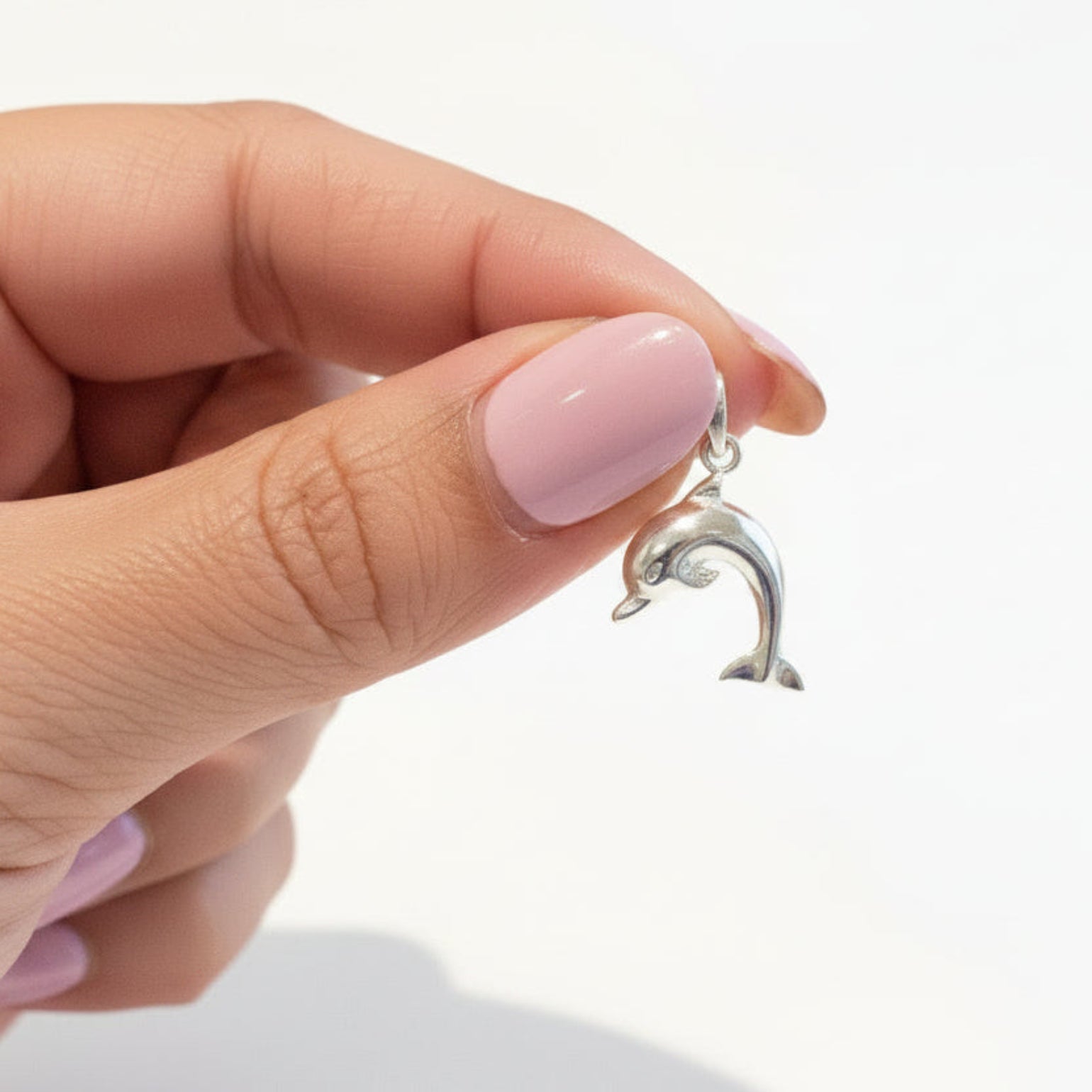 A silver dolphin pendant held between fingers. The pendant is made of polished silver metal with a small bail at the top for a chain.