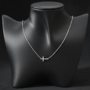 A delicate silver cross pendant necklace displayed on a matte black jewelry bust against a light gray background.