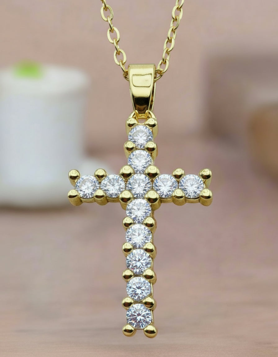 Gold cross pendant necklace with clear stones on a blurred background