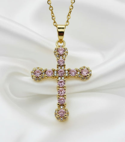 Gold cross pendant with pink gemstones on a white background