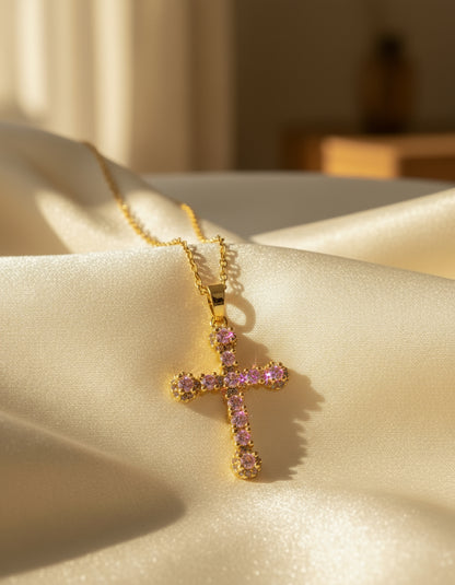 Gold cross pendant with pink gemstones on a white background