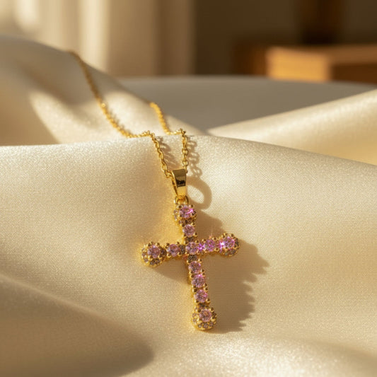 Gold cross pendant with pink gemstones on a white background