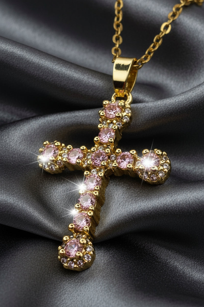 Gold cross pendant with pink gemstones on a white background