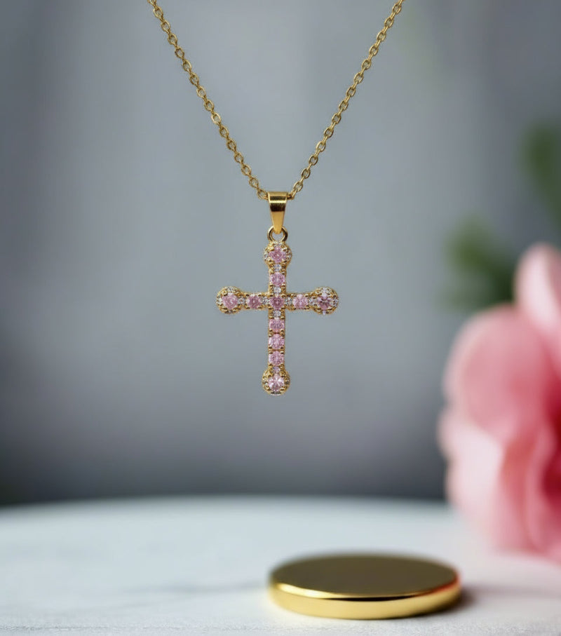 Gold cross necklace with pink stones on a white stand