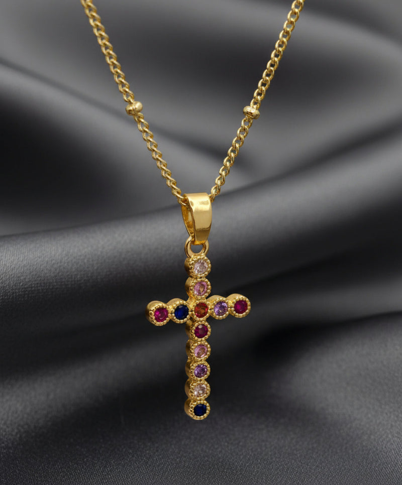 Gold cross pendant with colored gemstones on a light pink background