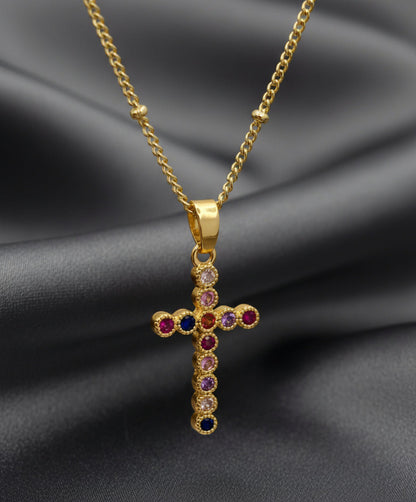 Gold cross pendant with colored gemstones on a light pink background