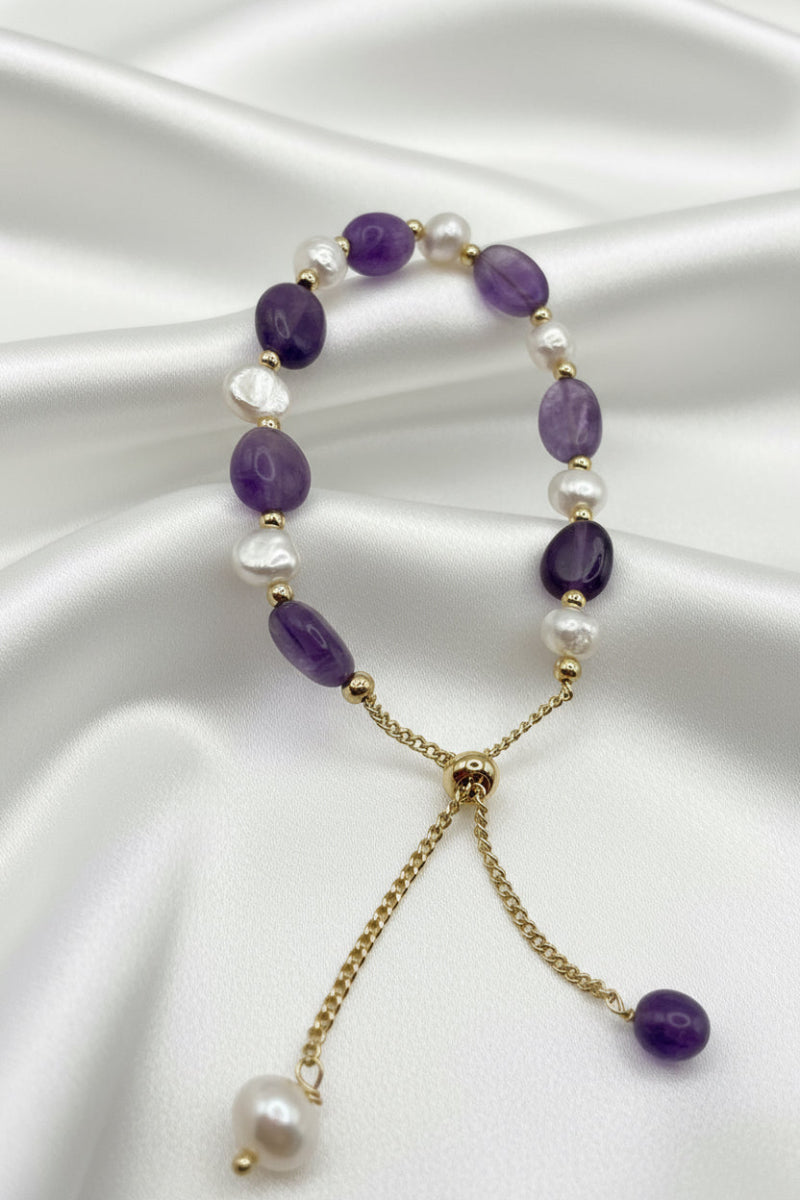 Beaded bracelet with purple and white beads on a gold chain, displayed on a white surface.