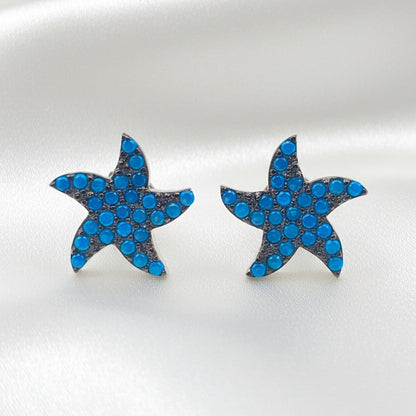 A pair of starfish-shaped stud earrings covered in small blue rhinestones with silver-toned edges, displayed on a plain white background.