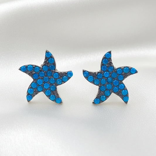 A pair of starfish-shaped stud earrings covered in small blue rhinestones with silver-toned edges, displayed on a plain white background.