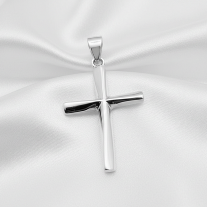A polished silver cross pendant with a smooth, reflective finish, resting on a draped white satin fabric background.