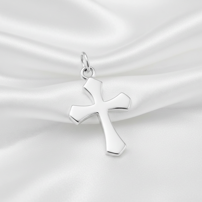 A polished silver cross pendant with a smooth, reflective finish, resting on draped white satin fabric.