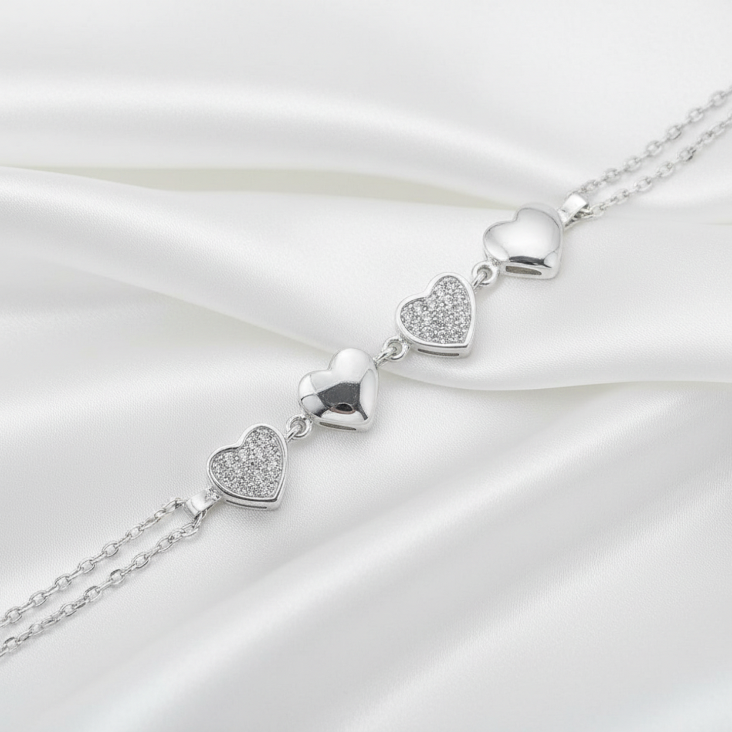 A silver heart-link chain bracelet featuring four polished and pavé-set heart charms, shown on a white background.