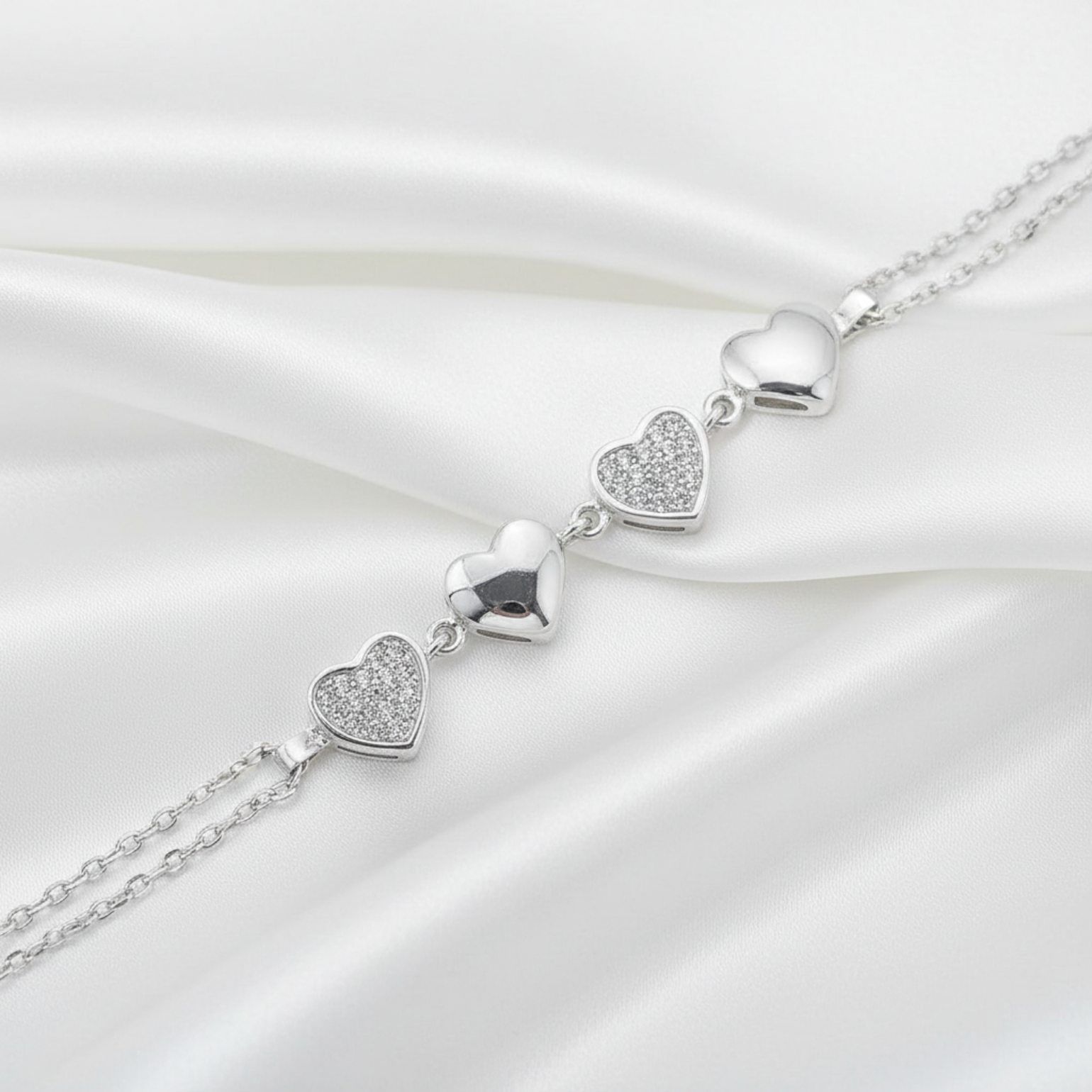 A silver heart-link chain bracelet featuring four polished and pavé-set heart charms, shown on a white background.