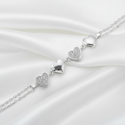A silver heart-link chain bracelet featuring four polished and pavé-set heart charms, shown on a white background.