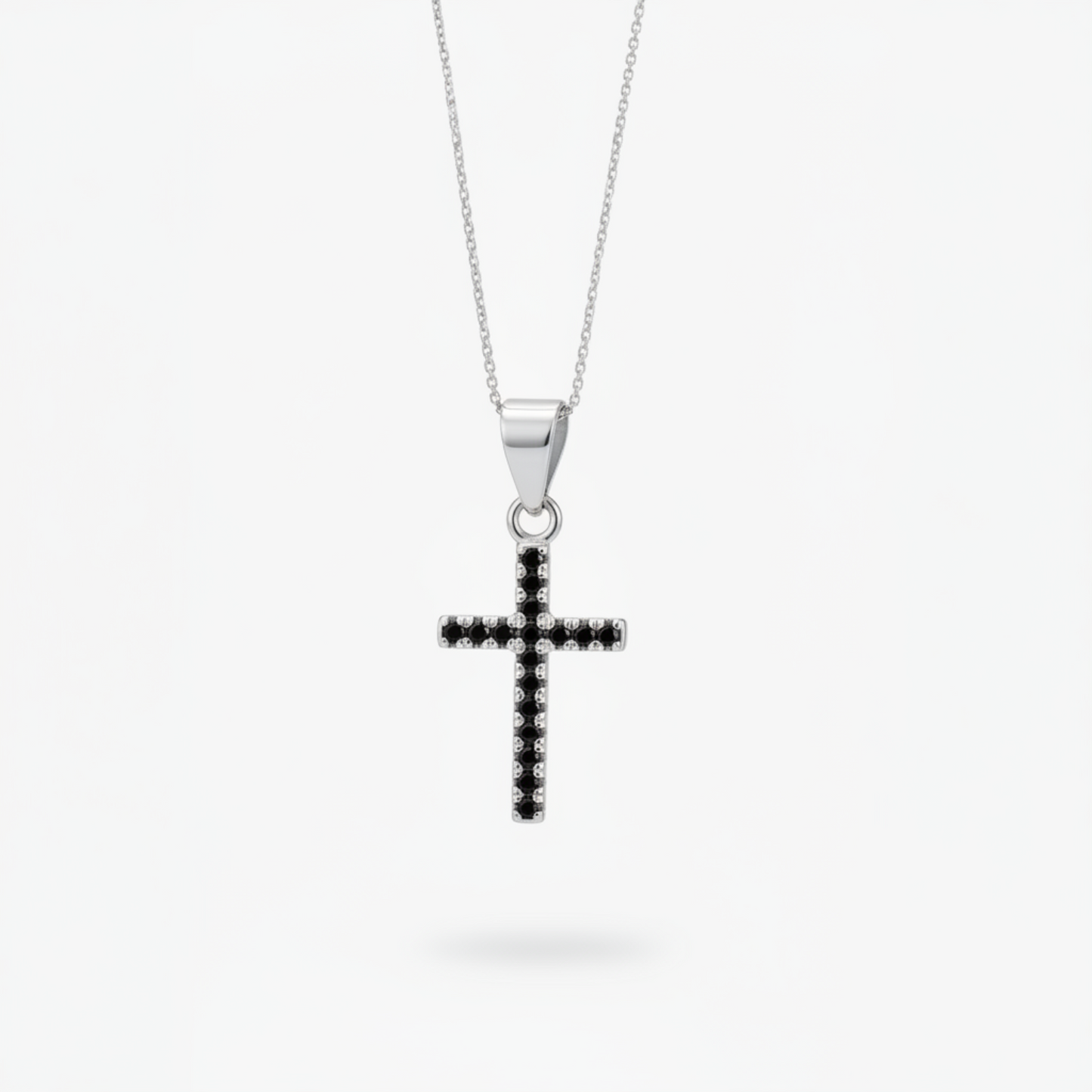 A silver cross pendant necklace with a row of small black stones, suspended from a delicate silver chain against a light gray background.