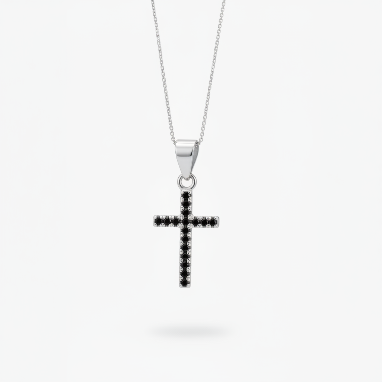 A silver cross pendant necklace with a row of small black stones, suspended from a delicate silver chain against a light gray background.