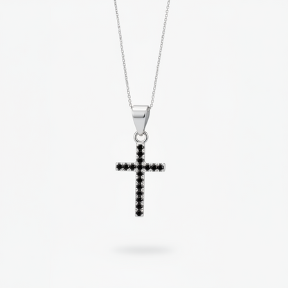 A silver cross pendant necklace with a row of small black stones, suspended from a delicate silver chain against a light gray background.