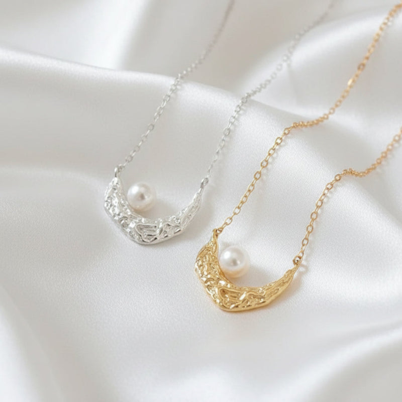 Two crescent moon-shaped necklaces with pearls on a neutral background
