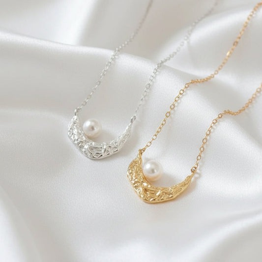 Two crescent moon-shaped necklaces with pearls on a neutral background
