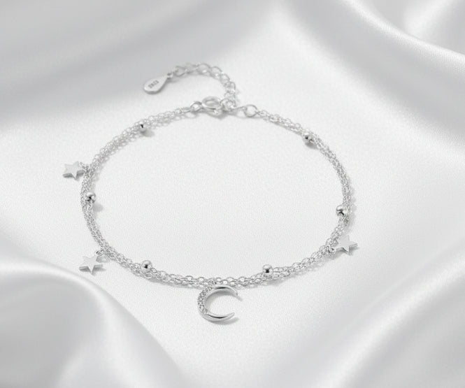 Silver bracelet with star and moon charms on a white background