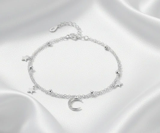 Silver bracelet with star and moon charms on a white background