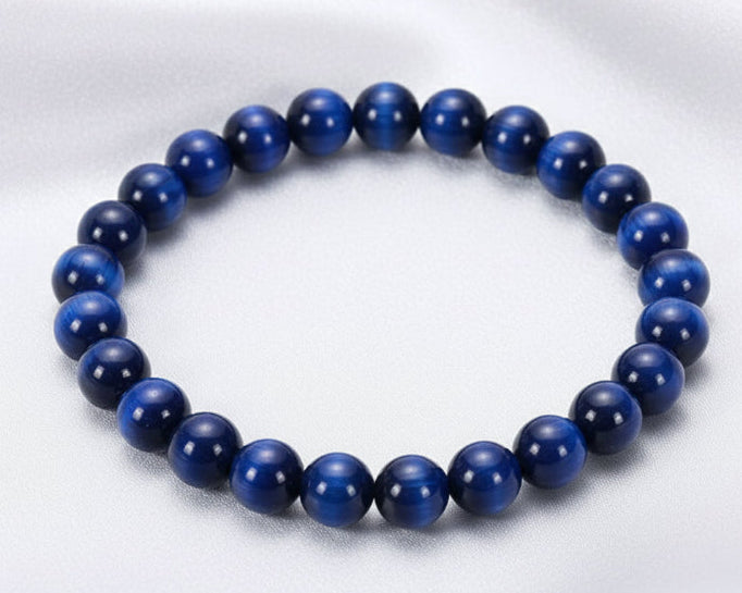 Blue beaded bracelet on a white surface with a stone in the background
