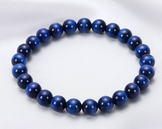 Blue beaded bracelet on a white surface with a stone in the background