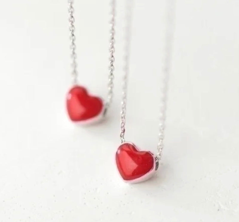 Two red heart-shaped pendants on silver chains against a white background