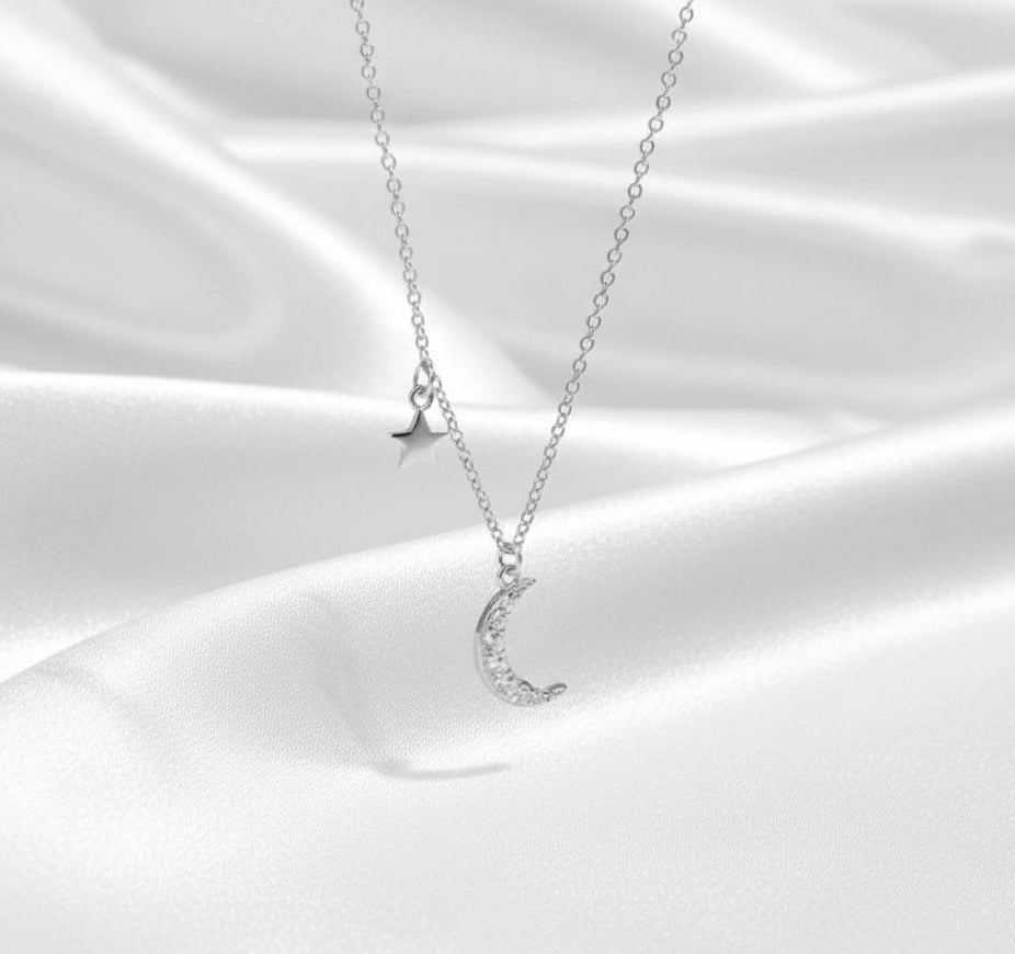 Silver necklace with moon and star pendants on a white satin background