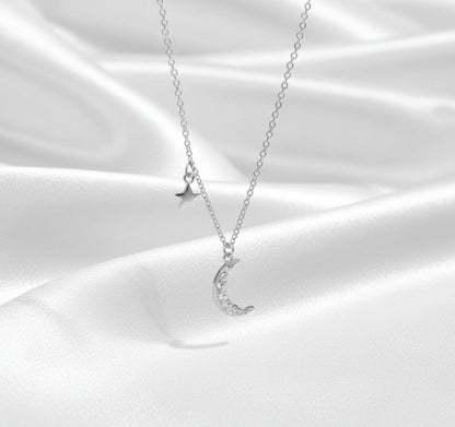 Silver necklace with moon and star pendants on a white satin background