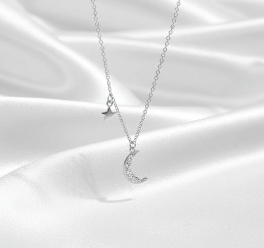 Silver necklace with moon and star pendants on a white satin background
