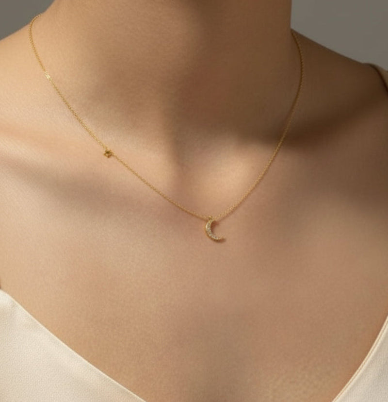 Gold necklace with a moon pendant on a person wearing a  white top.