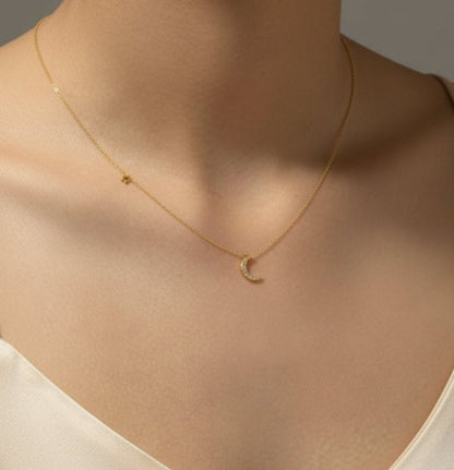 Gold necklace with a moon pendant on a person wearing a  white top.