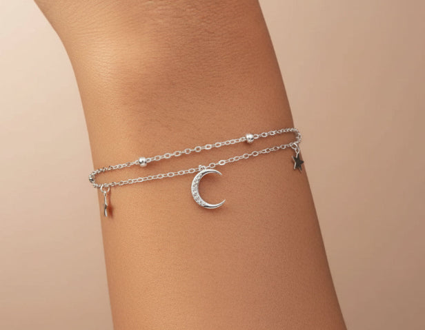 Silver anklets with moon designs on a person's ankle against a neutral background